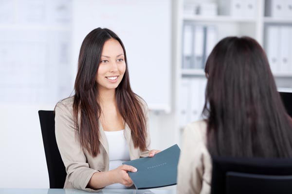 A young woman passes her resume to an interviewer